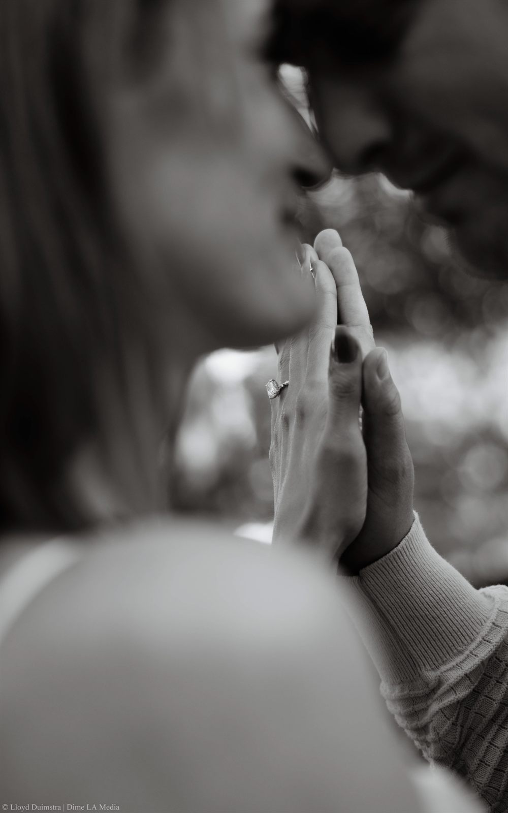 Black and white close-up of a couple's hands pressed together showing an engagement ring