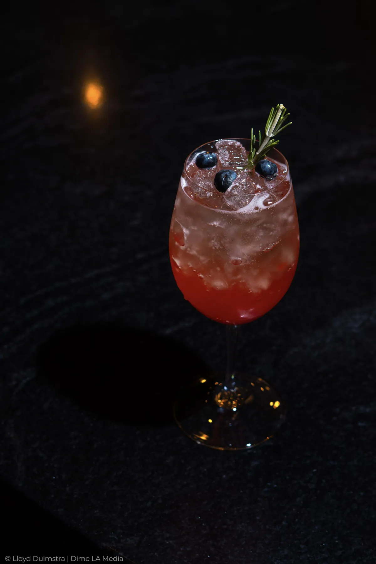 Berry spritz in a wine glass with blueberries and a rosemary sprig on black stone