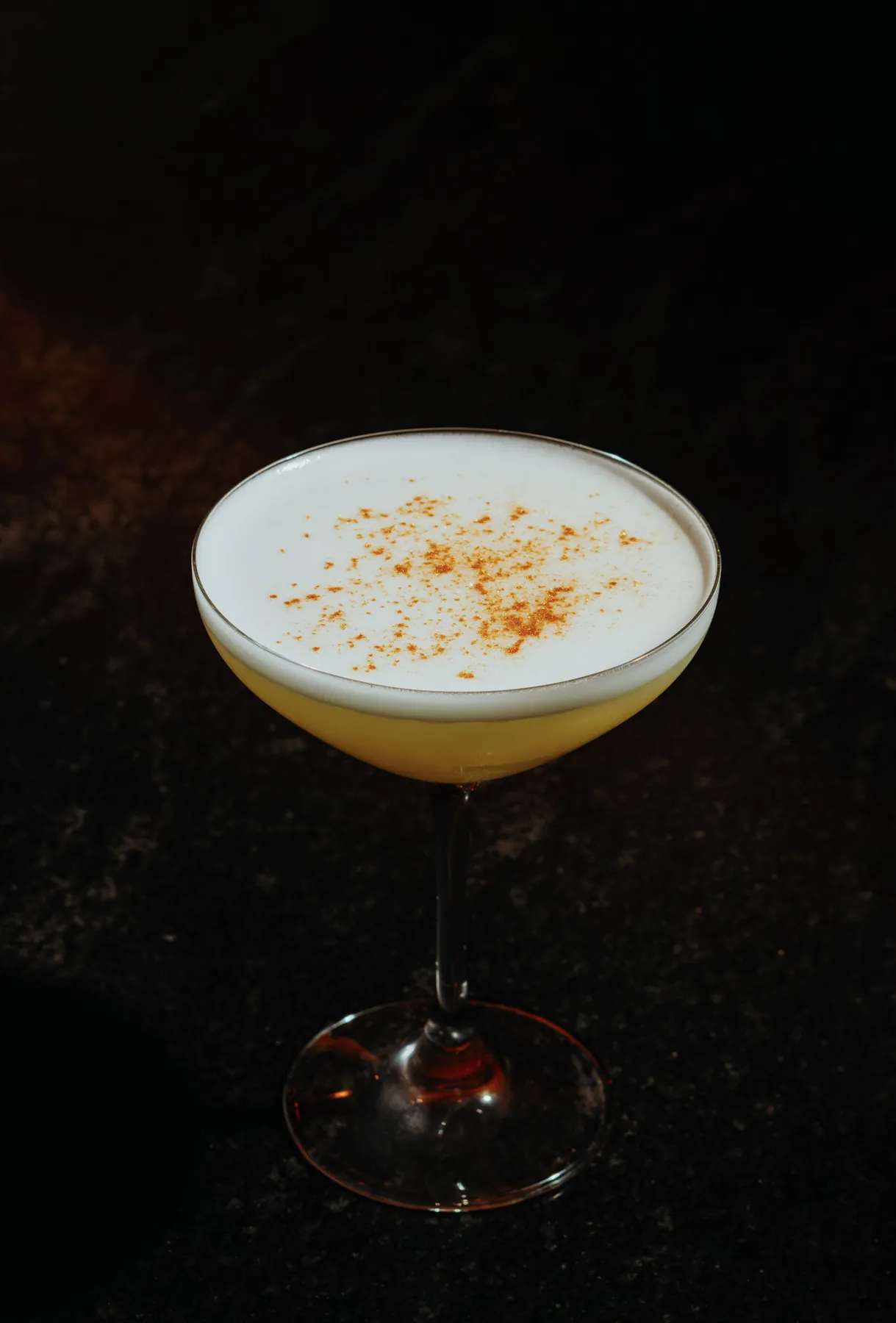 Whiskey sour served up in a coupe with a smooth foam top dusted with cinnamon