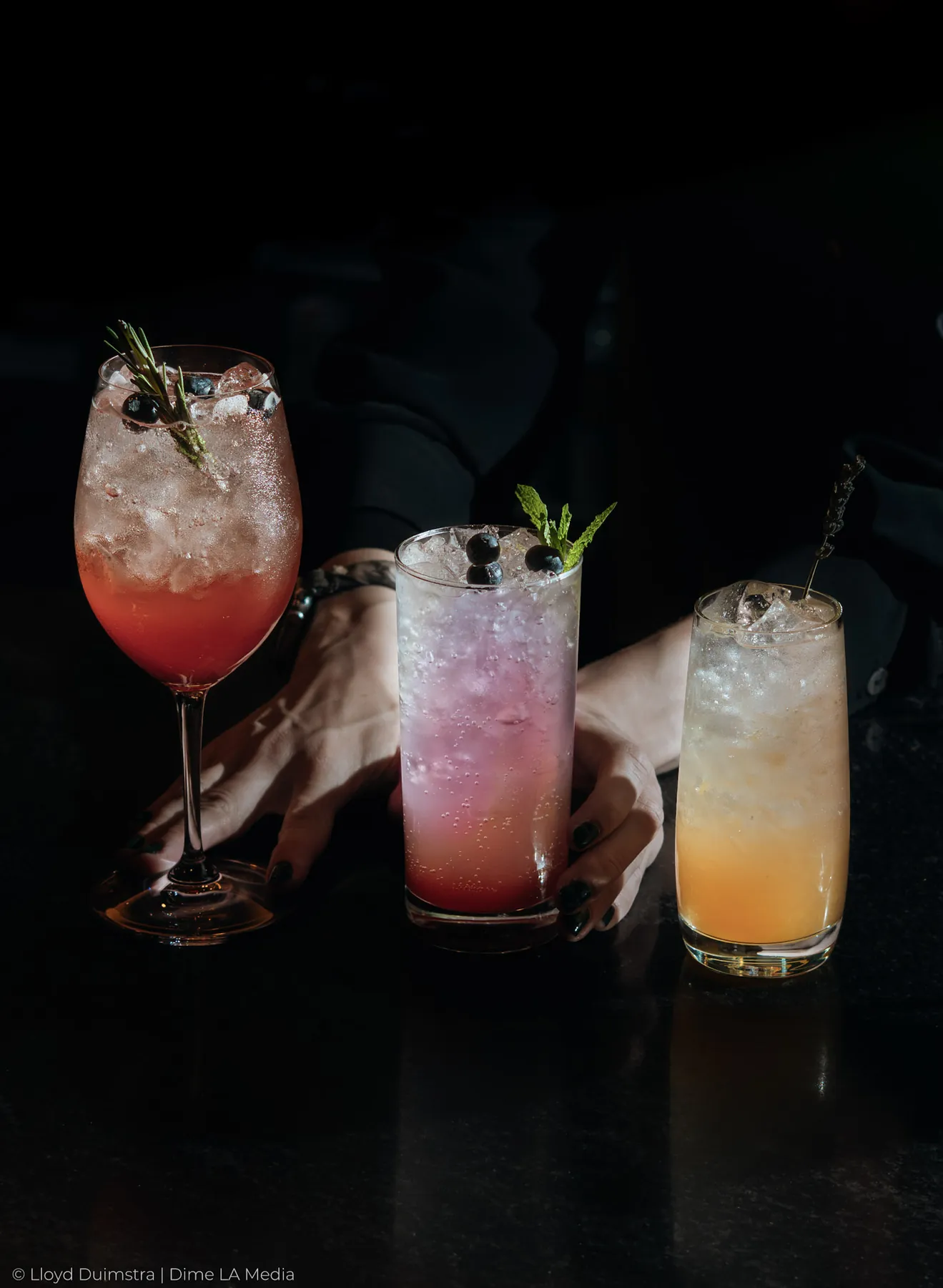 Three cocktails served together as a bartender sets them down on the bar