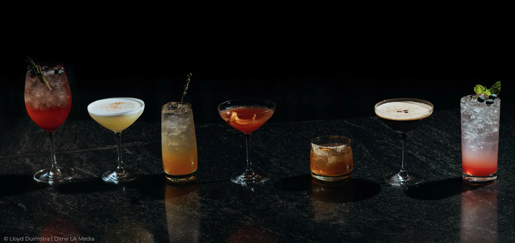A full lineup of seven signature cocktails along a dark bar top, Sioux Falls SD