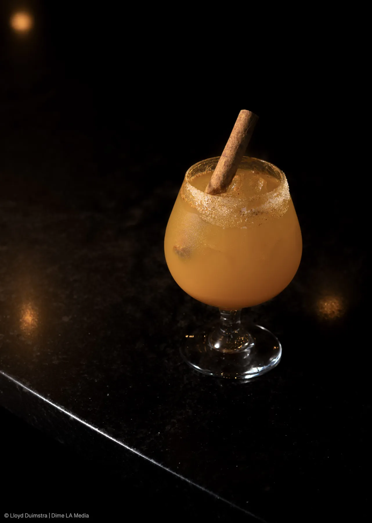 Spiced amber cocktail with a cinnamon stick and a sugared rim on a dark bar