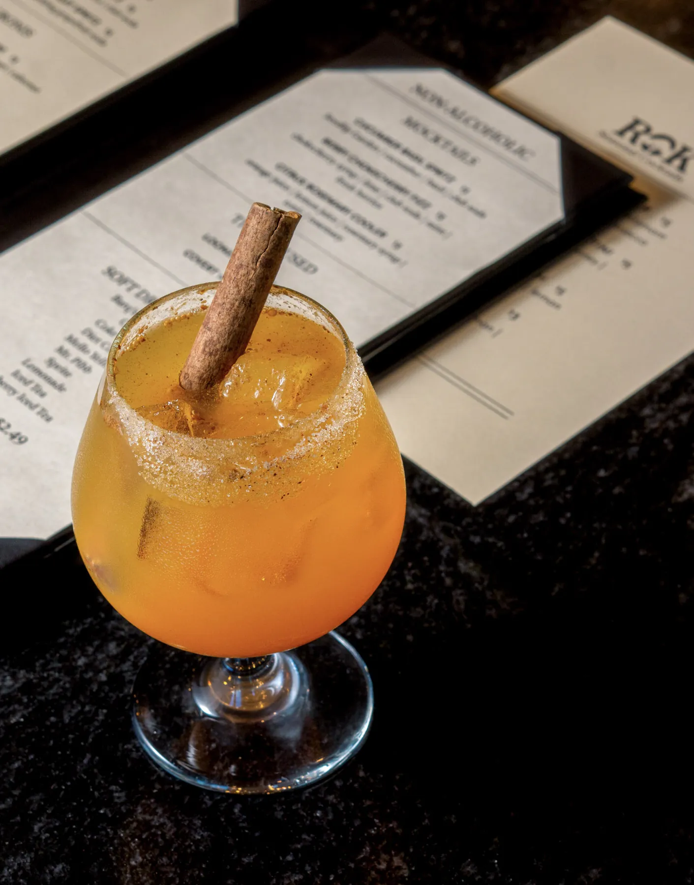 Cinnamon-garnished amber cocktail beside a seasonal cocktail menu