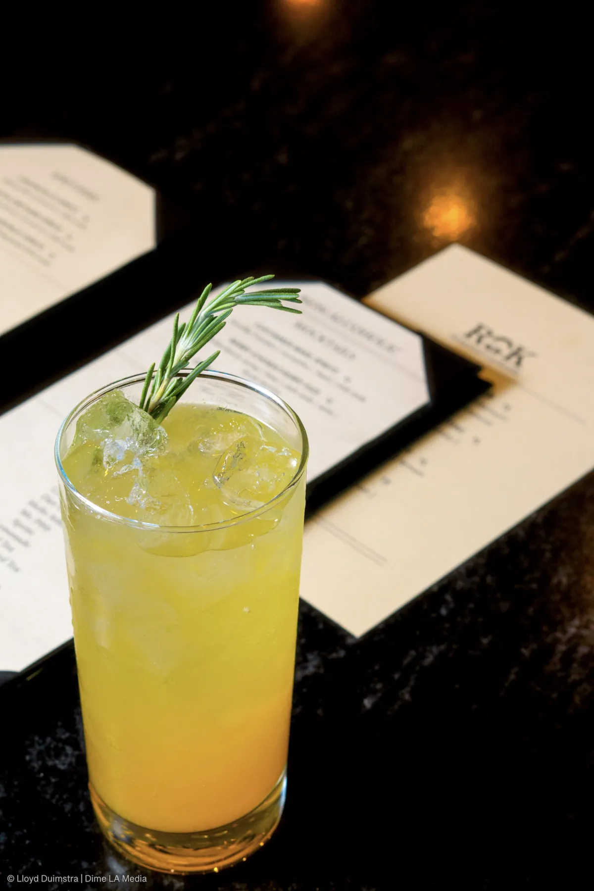 Bright citrus highball with a rosemary sprig beside a seasonal cocktail menu