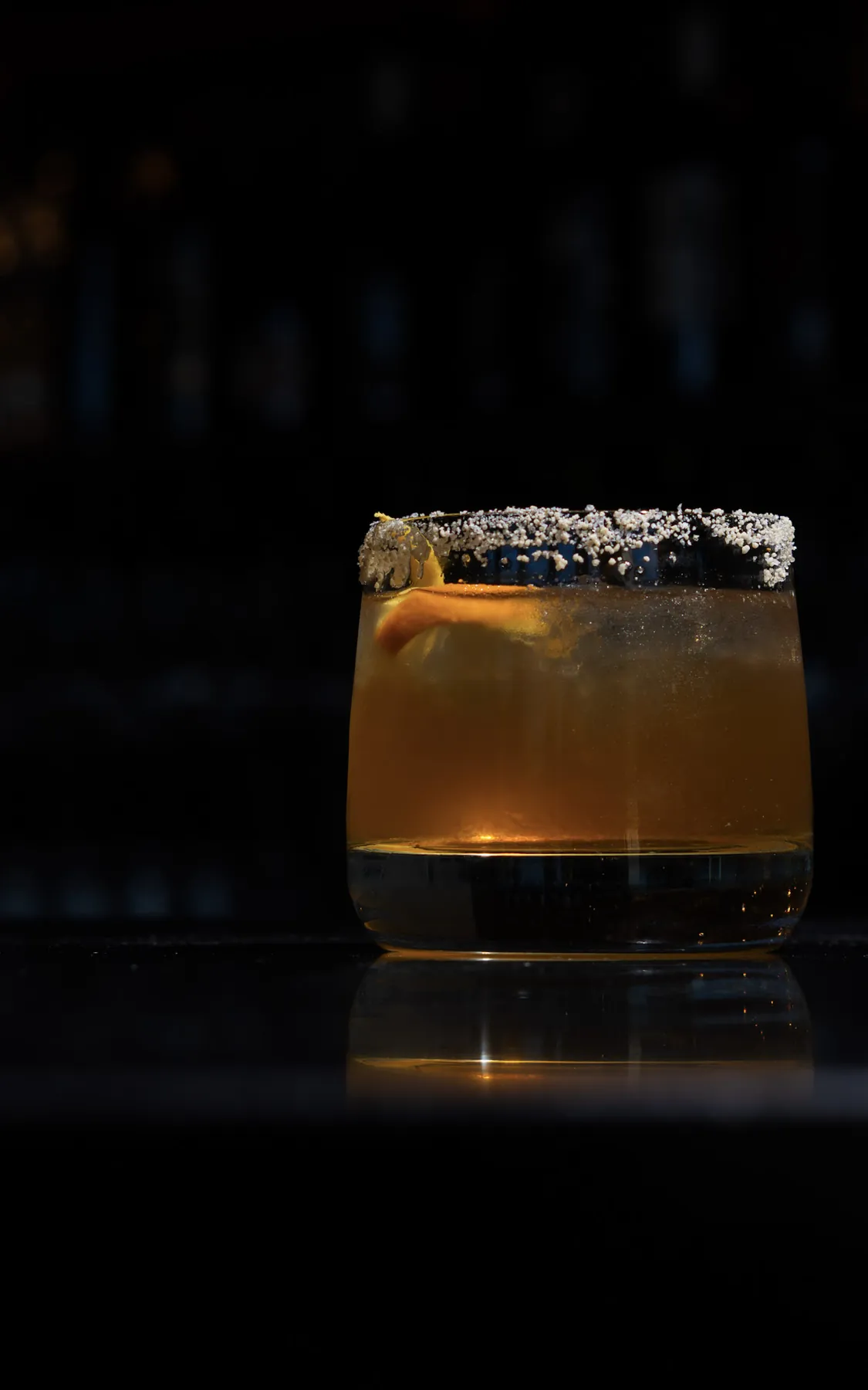 Old fashioned in a rocks glass with a sugared rim, backlit against the back bar