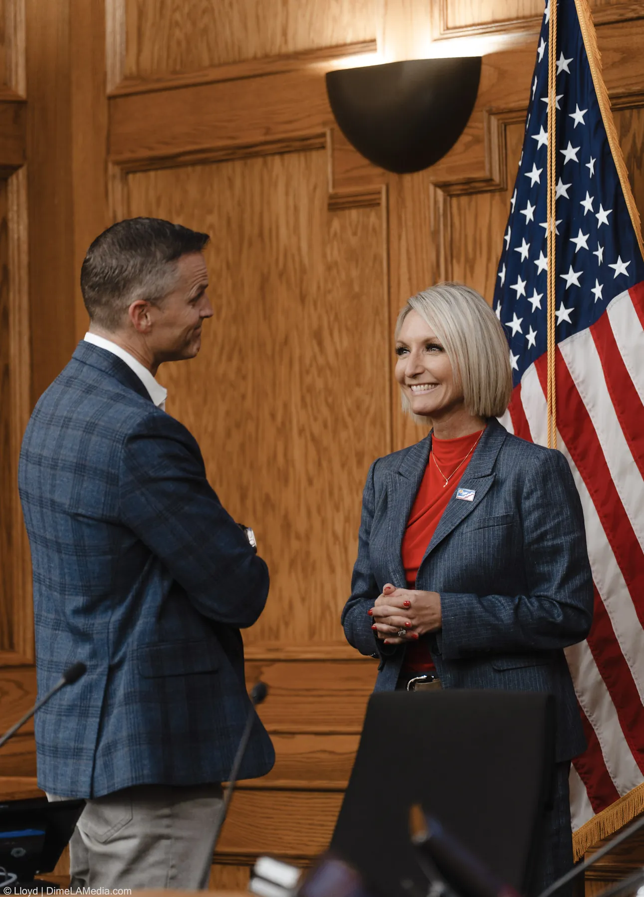 Christine Erickson smiles in conversation with Paul TenHaken beside the flag before the ceremony