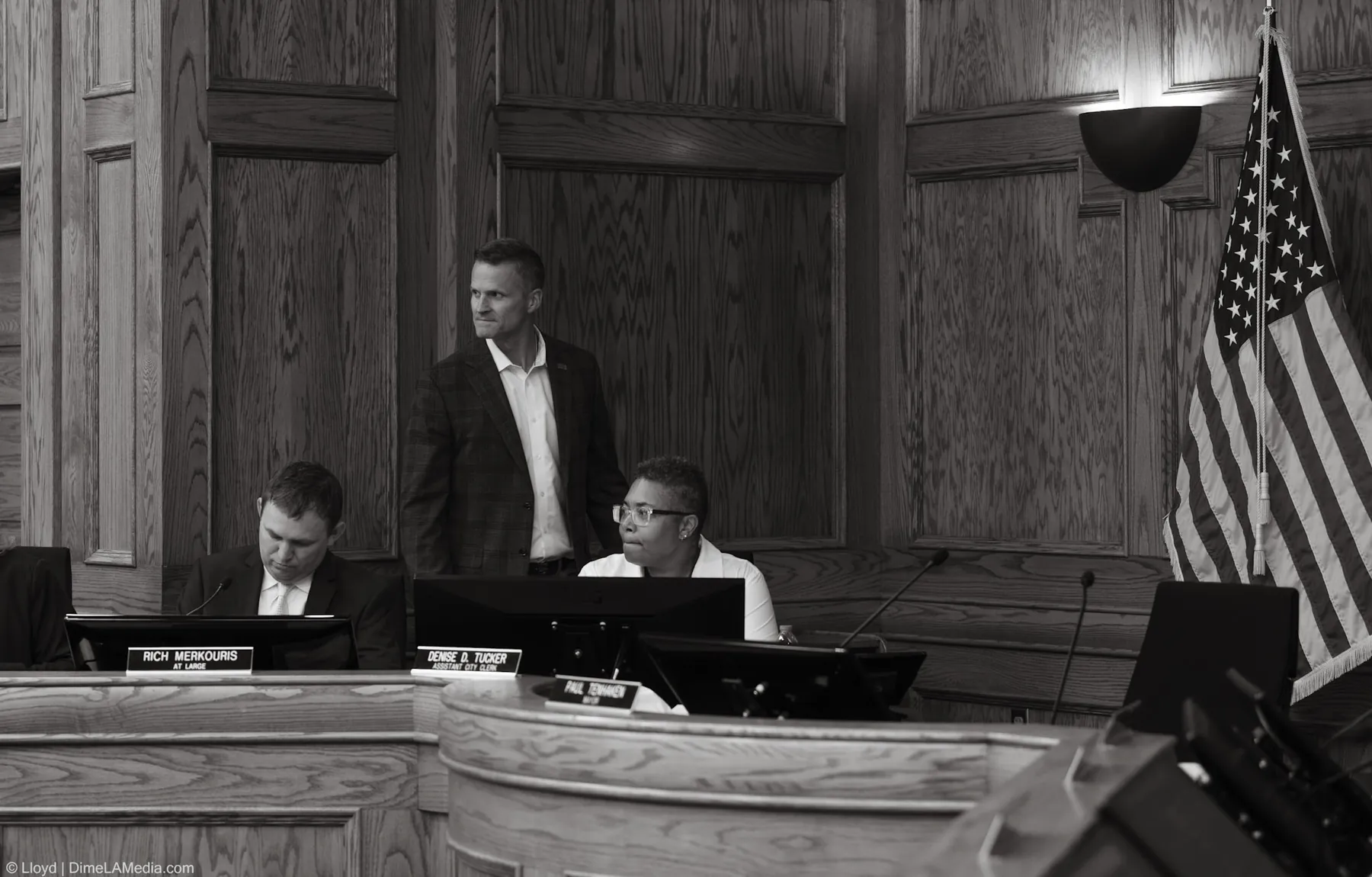Black and white frame of Paul TenHaken standing at the council dais behind his mayor nameplate for the final time