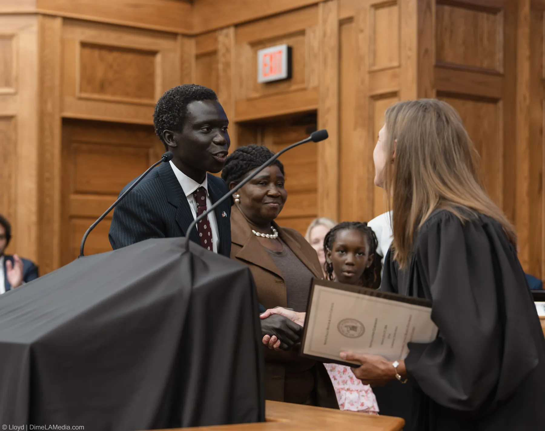 Zak Okuwe shakes hands with the presiding judge and receives his certificate as his family looks on