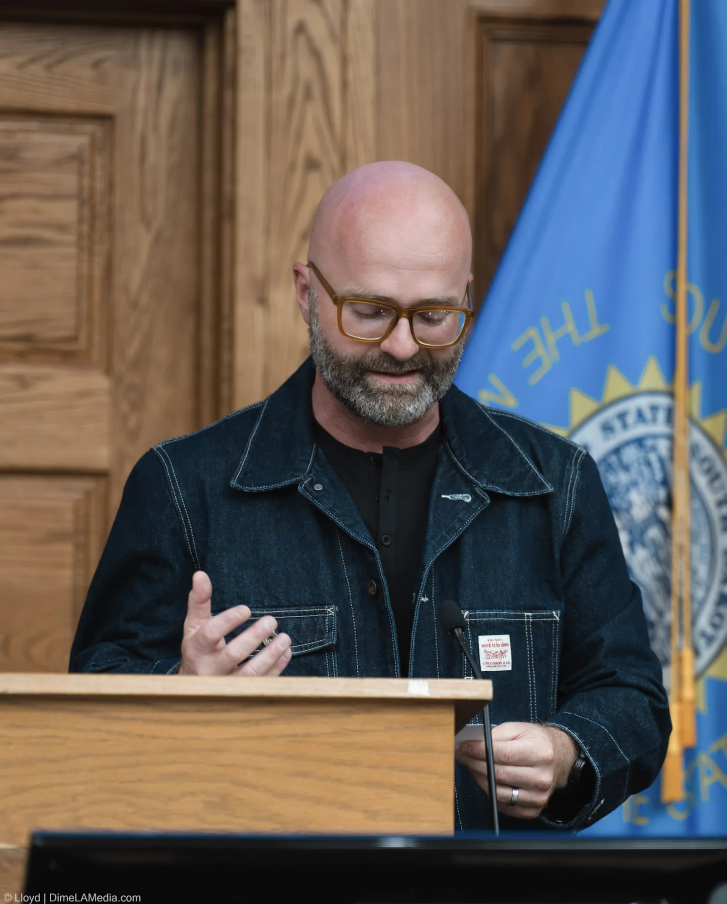 Pastor Adam Weber speaks at the podium in front of the South Dakota flag