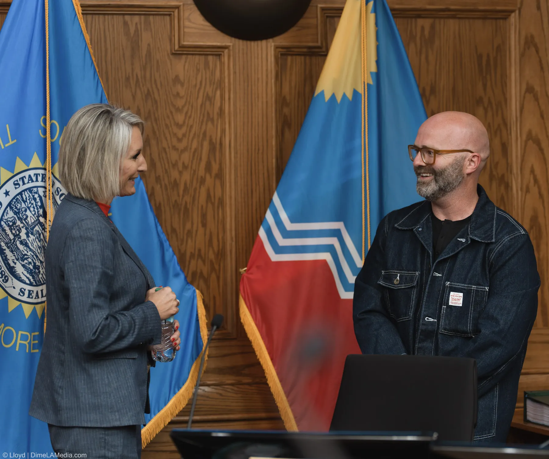 Mayor Christine Erickson and Pastor Adam Weber share a laugh beside the flags after the ceremony