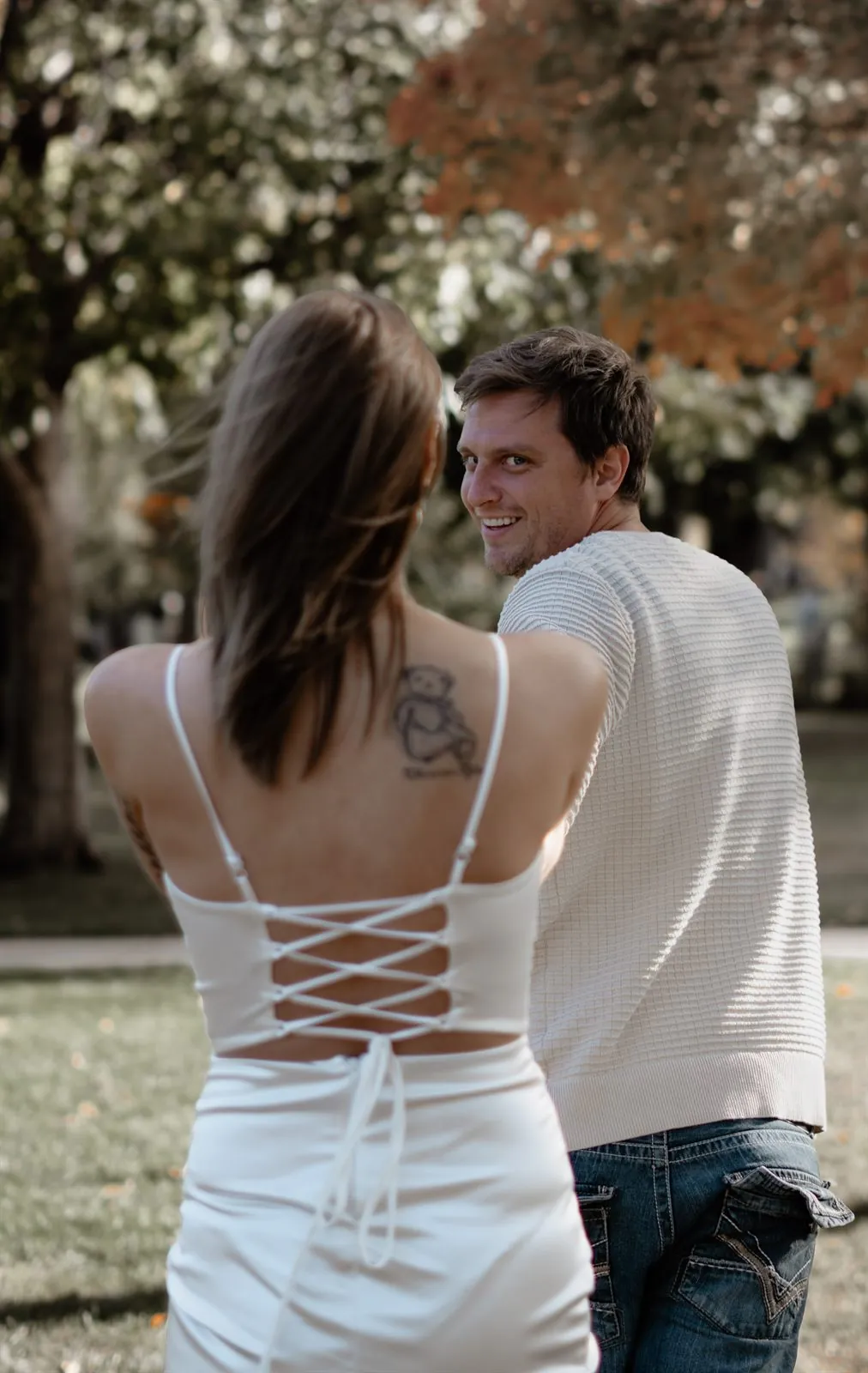 Couple walking through an autumn park, groom glancing back with a smile