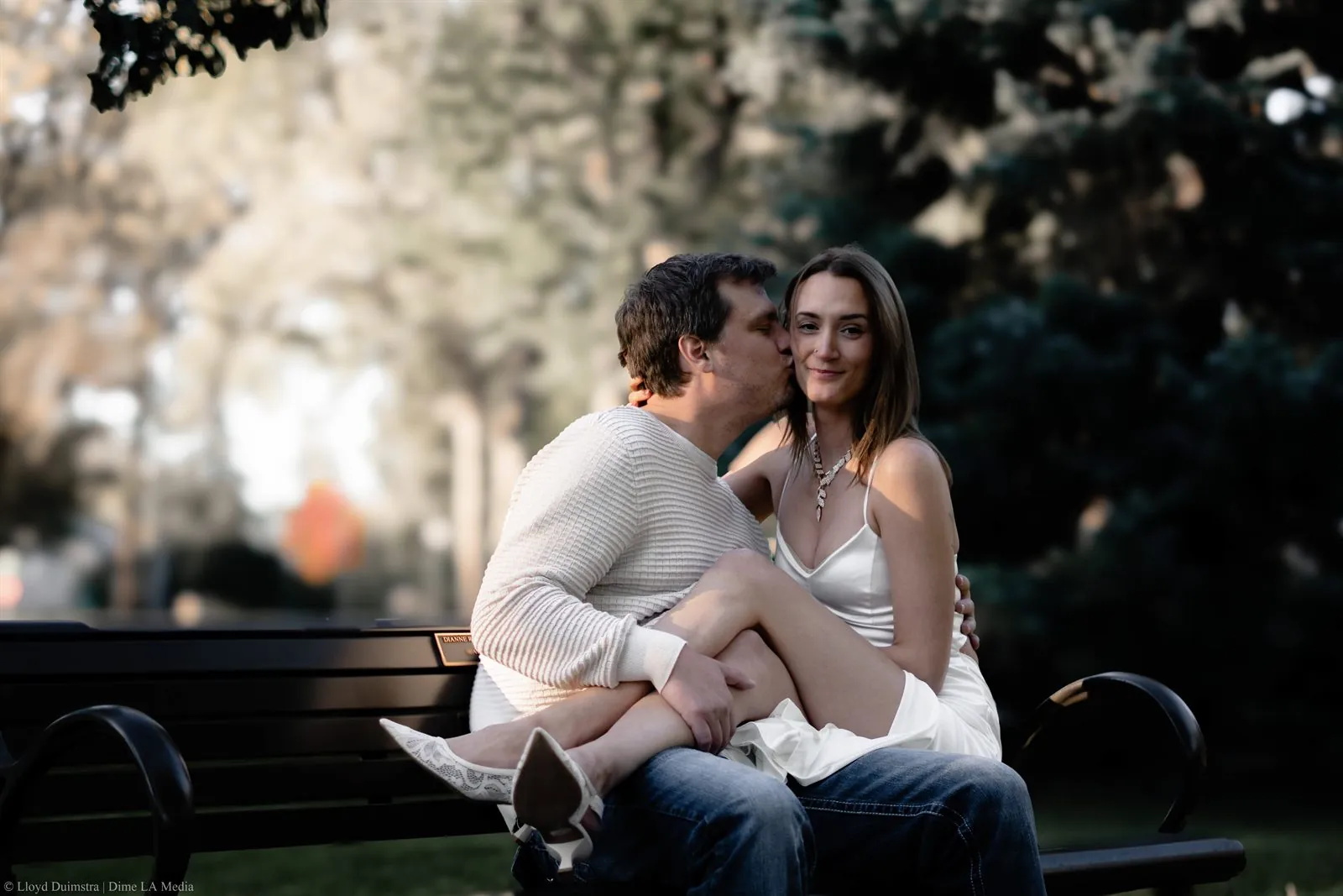 Man kissing his fiancee's temple on a bench in an autumn park