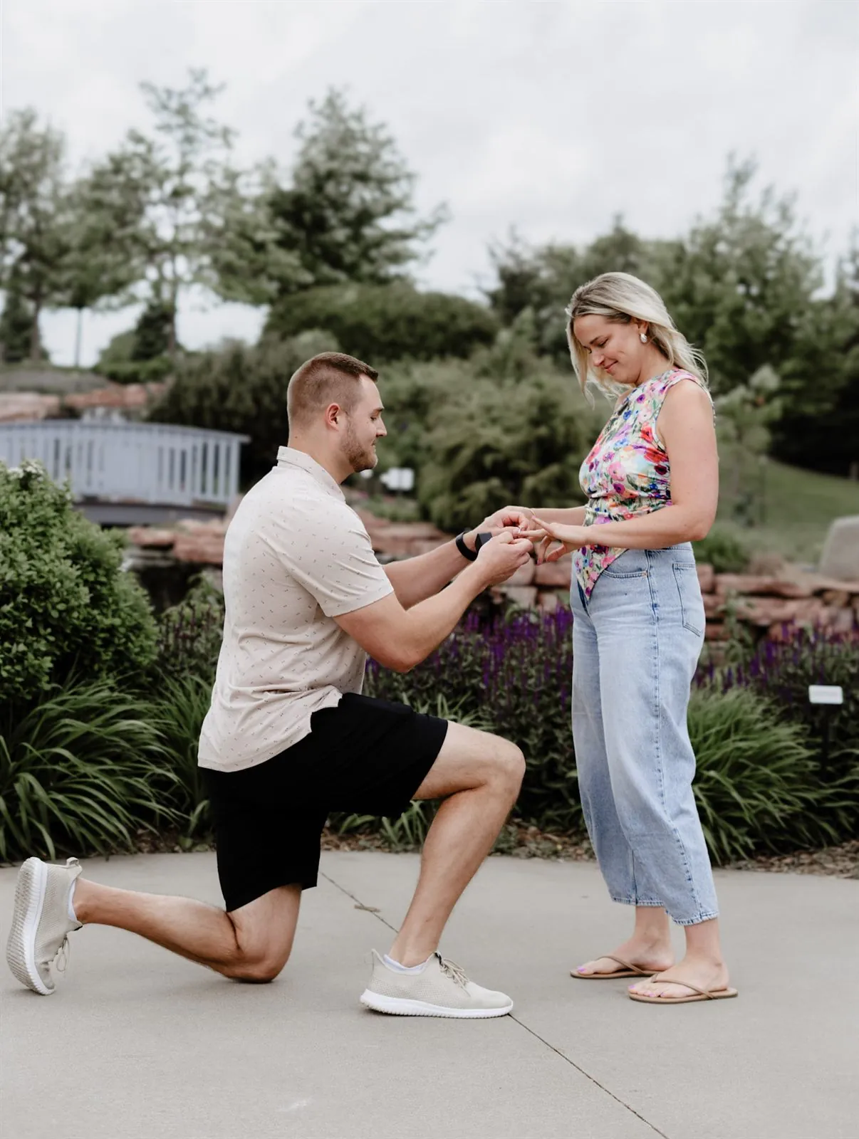 Man on one knee proposing and placing a ring on his partner's finger in a garden