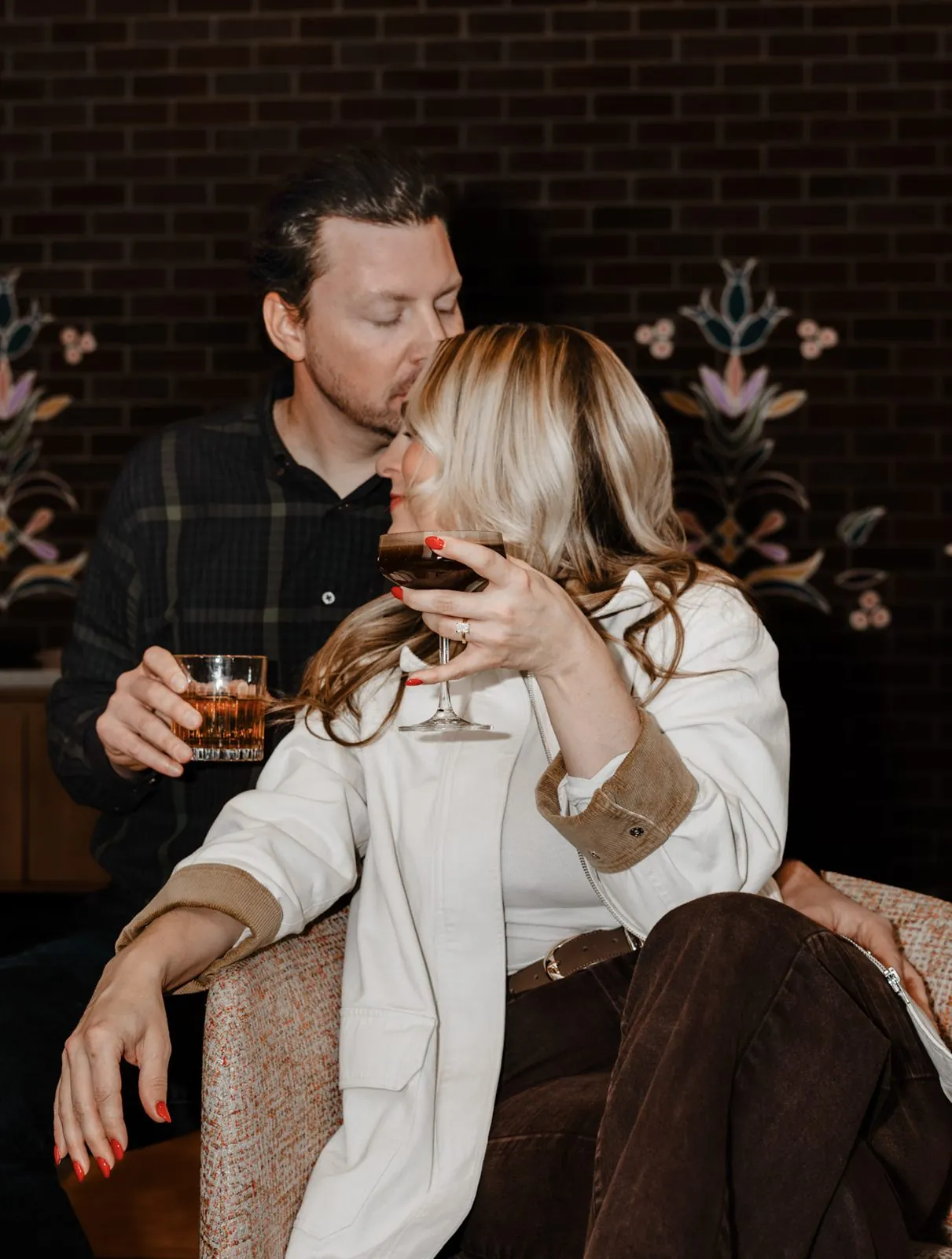 Man kissing his partner's head as she sips an espresso martini at a cozy bar