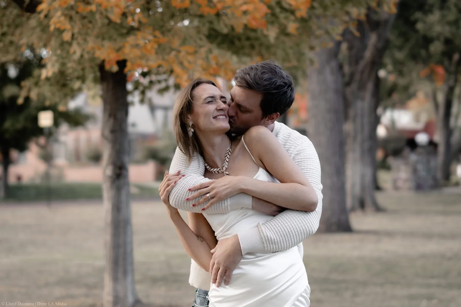 Couple embracing and laughing beneath golden fall foliage