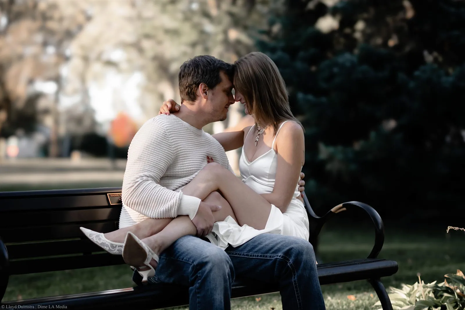 Engaged couple sitting together on a park bench, foreheads touching