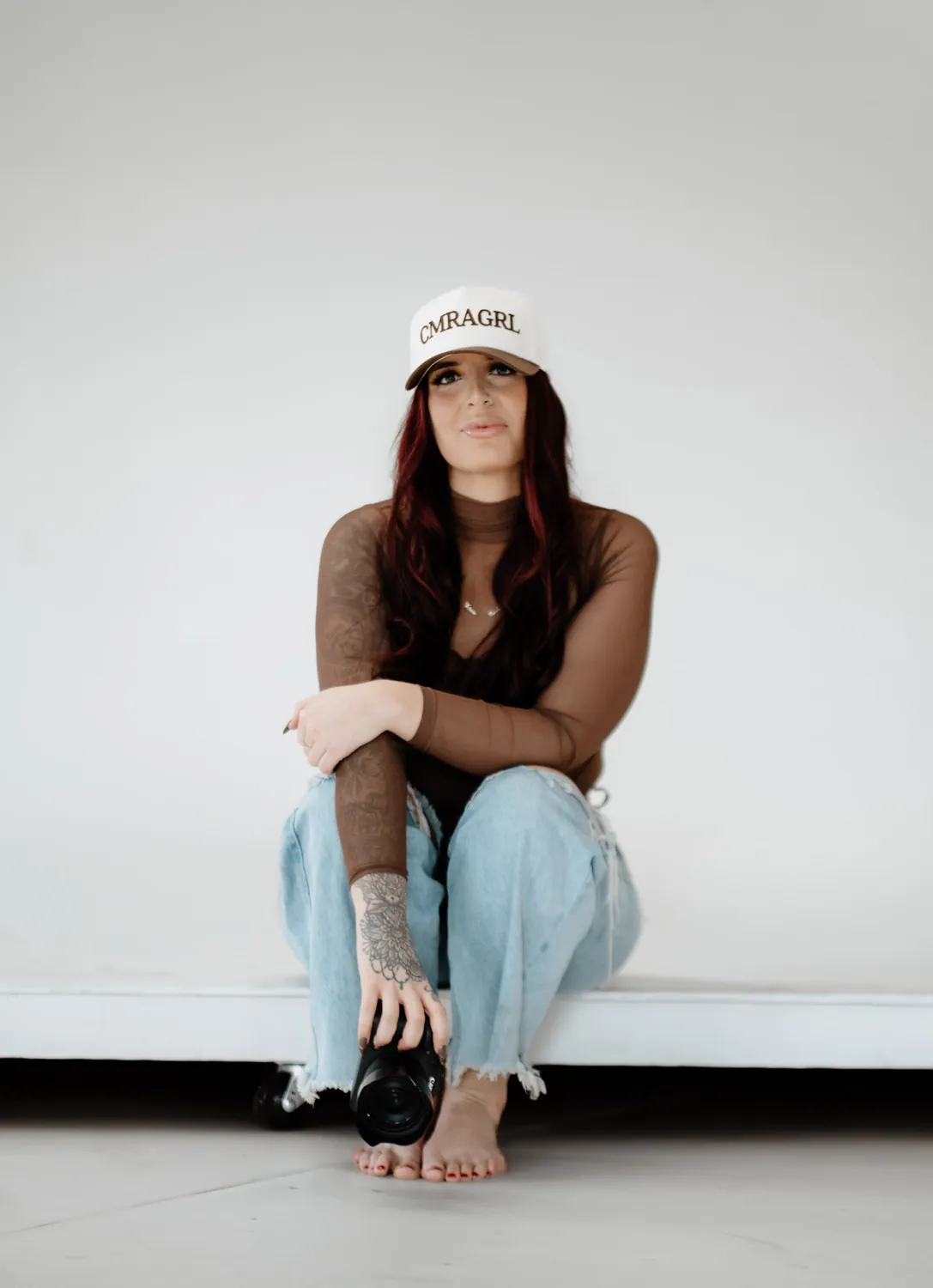 Jade sits on the edge of the white studio backdrop with her camera, personal brand photography by Dime LA Media