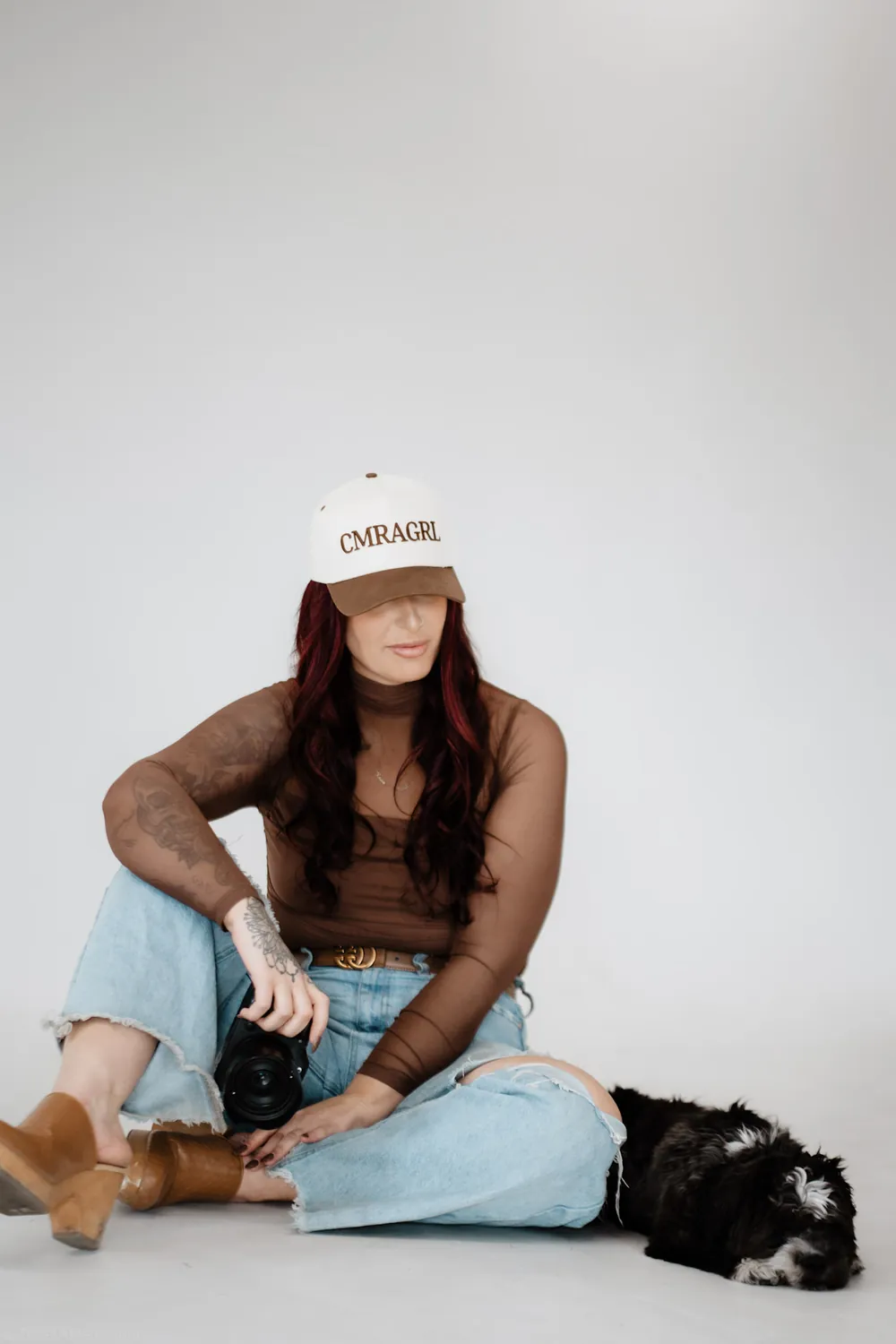 Jade with her hat pulled low over her eyes, seated on the white studio backdrop