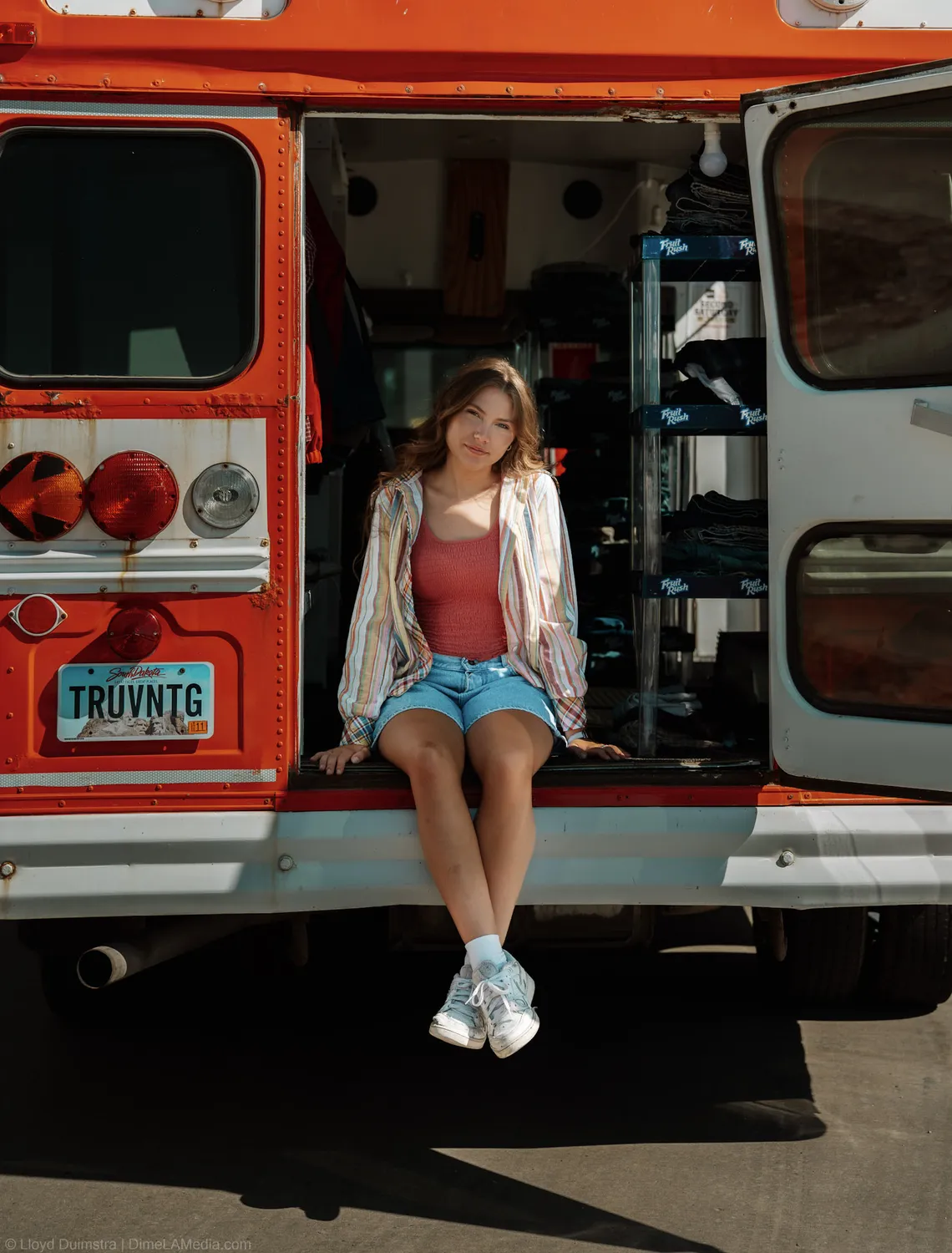 Maddie Theisen sits on the tailgate of the True Vintage bus with the TRUVNTG plate below her