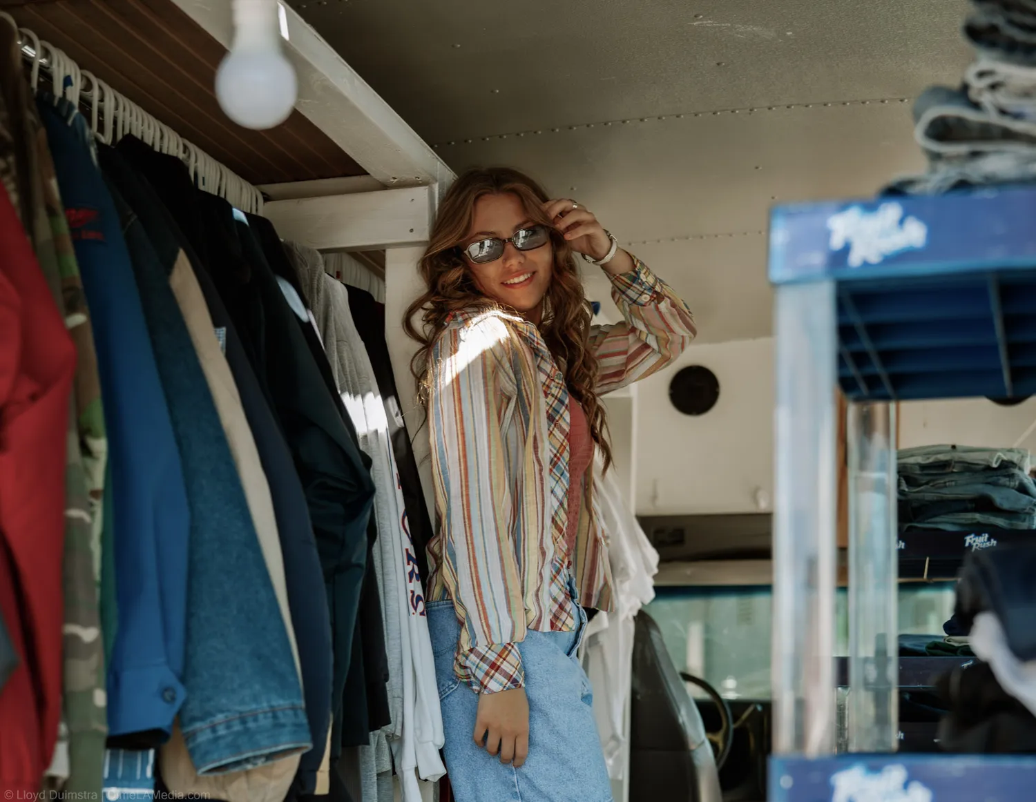 Maddie Theisen adjusts her sunglasses beside racks of vintage clothing inside the bus
