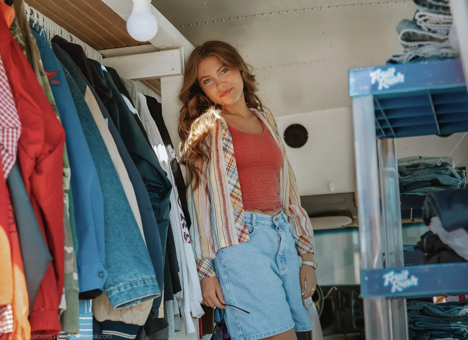 Maddie Theisen stands among hanging denim jackets and vintage pieces inside the True Vintage bus