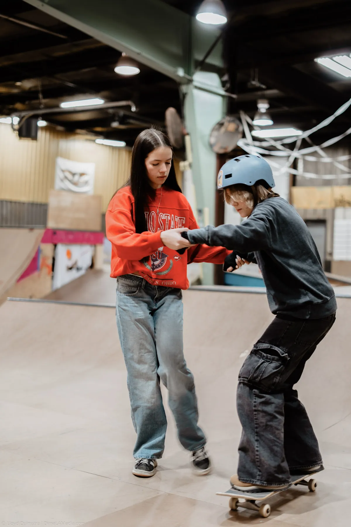 Instructor guiding a young skater across an indoor ramp