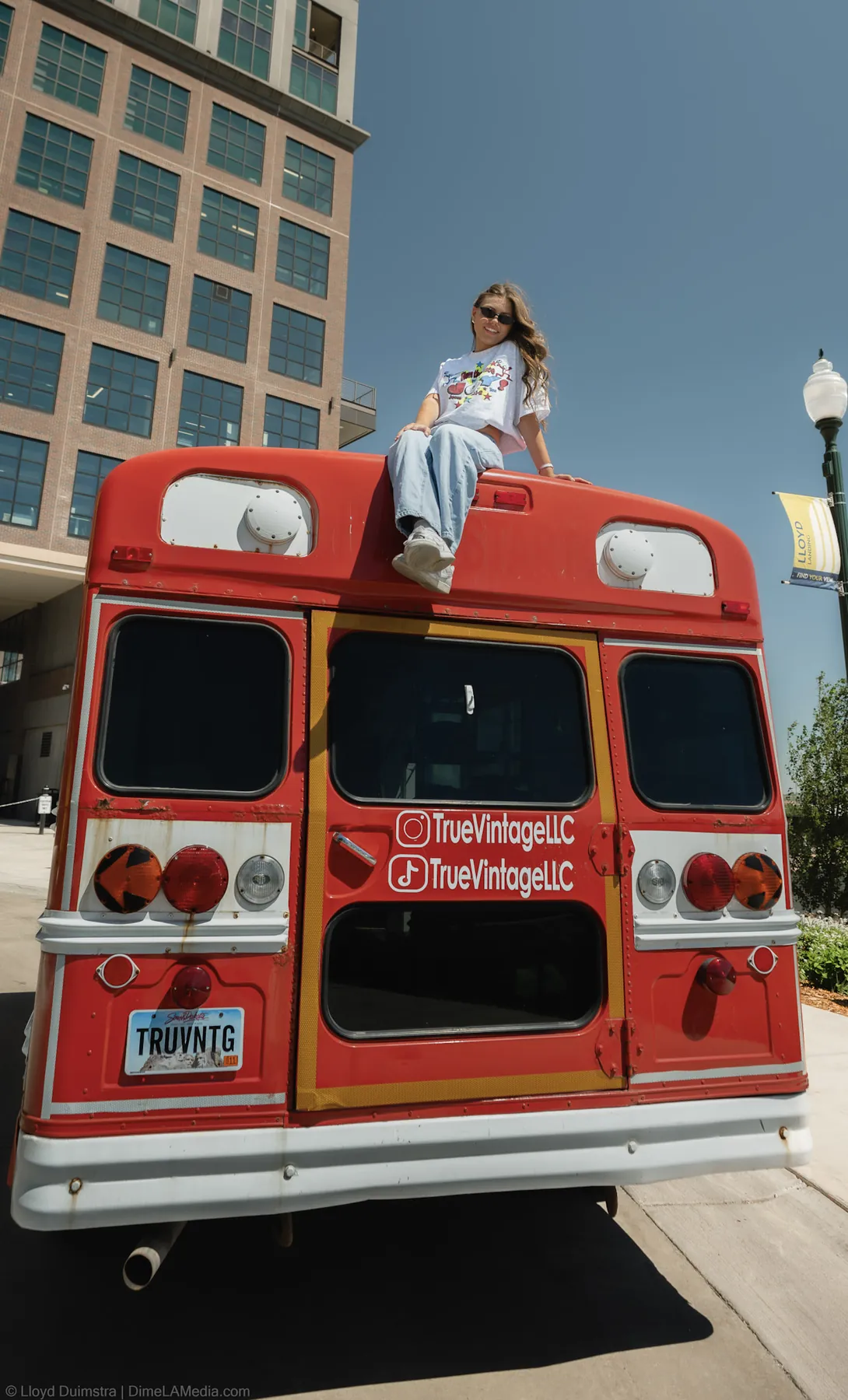 Maddie of True Vintage LLC sitting on the roof of her red vintage clothing bus in the Steel District, Sioux Falls SD