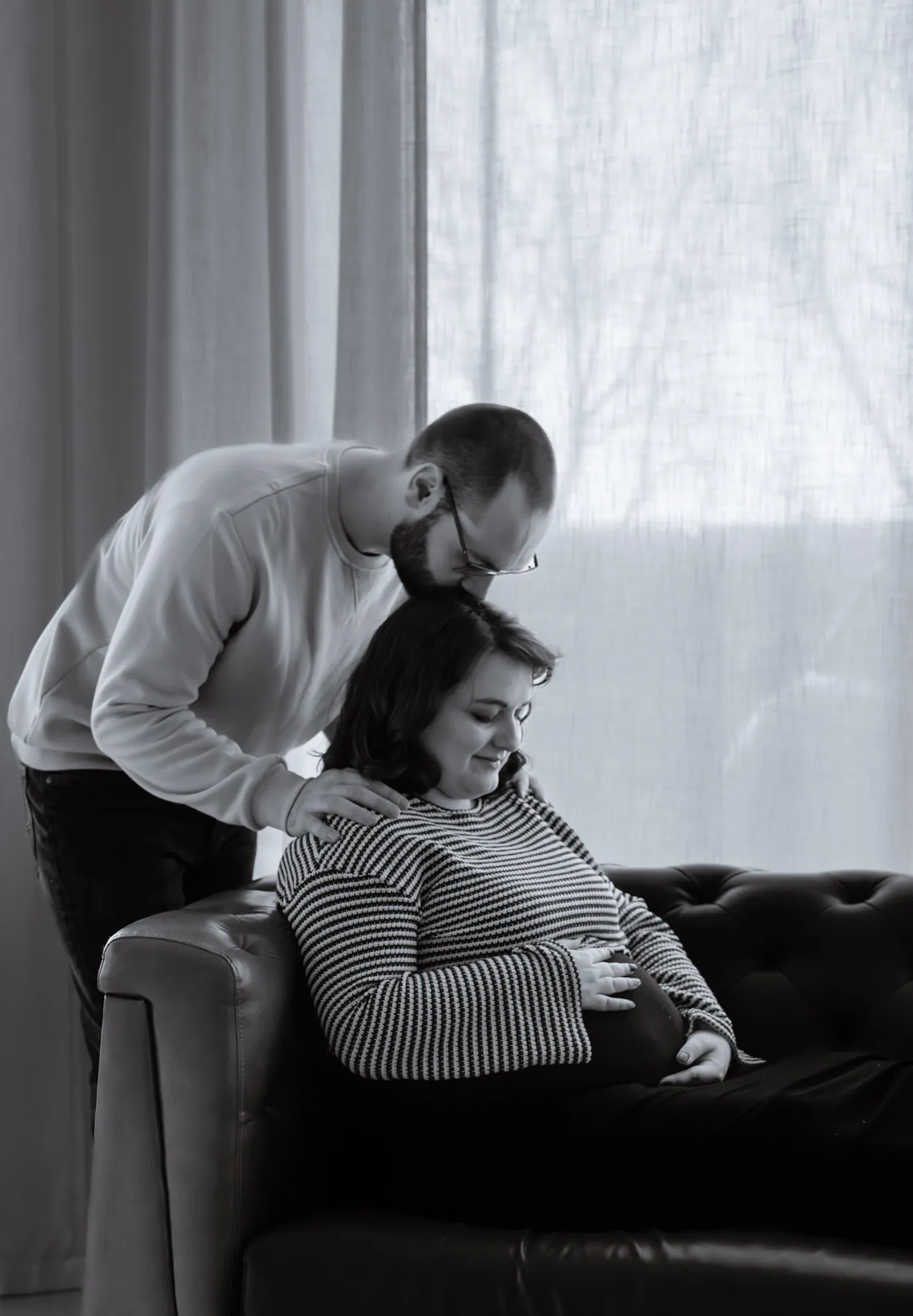 Dad leaning over the couch to kiss mom during the maternity session