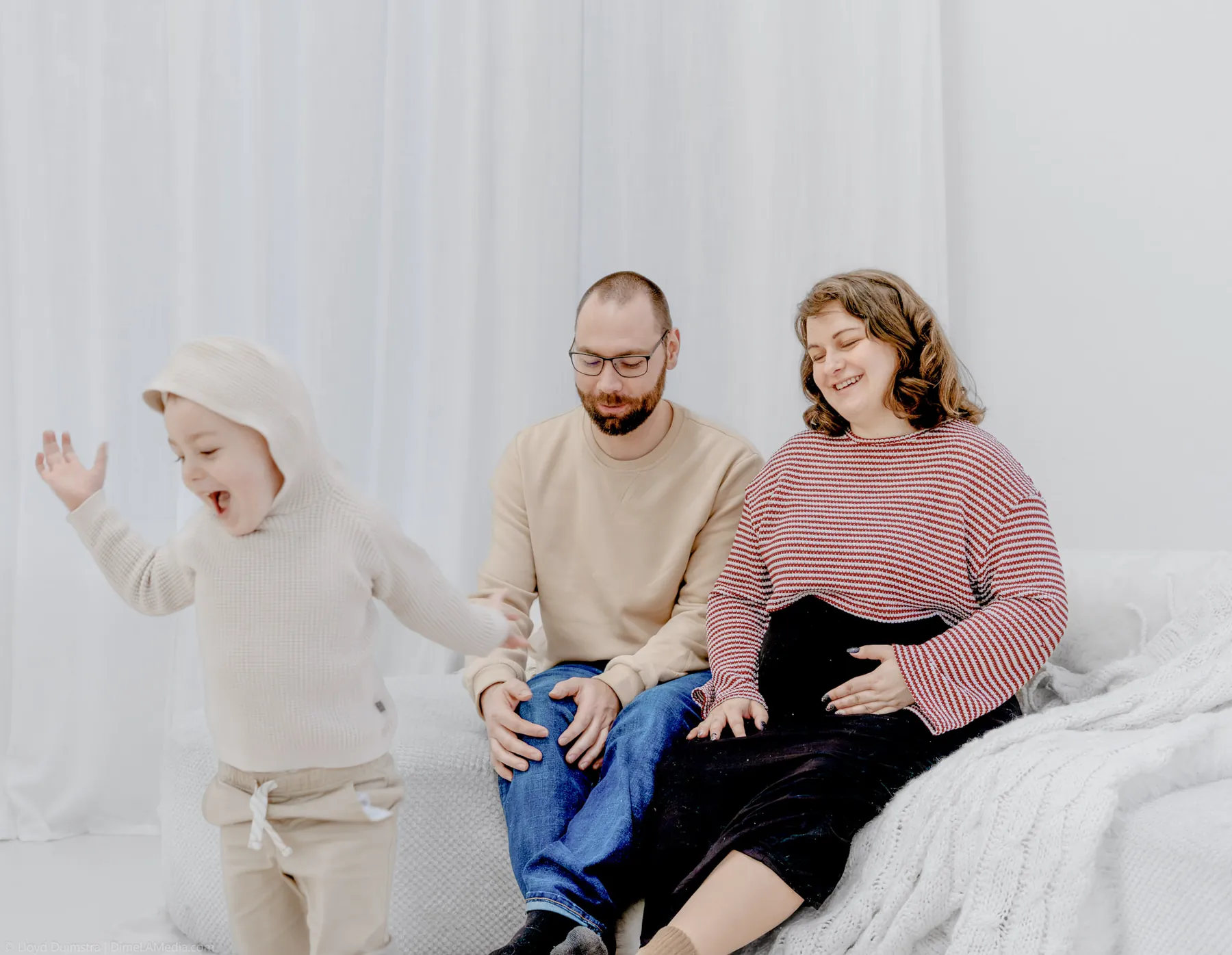 Toddler snuggled between his parents on the studio bed