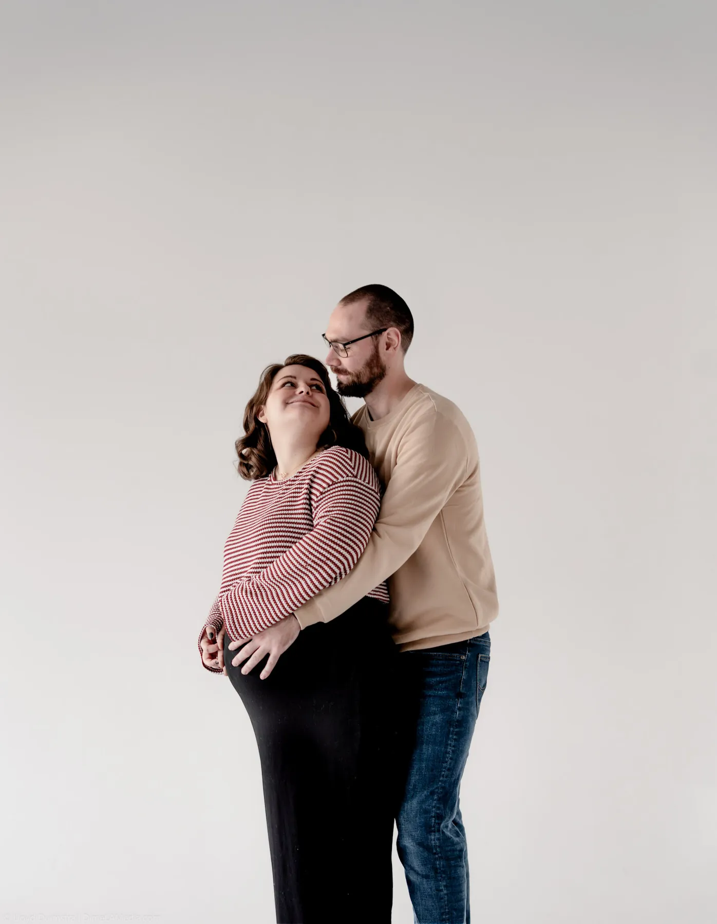Expecting parents embracing in a bright white studio