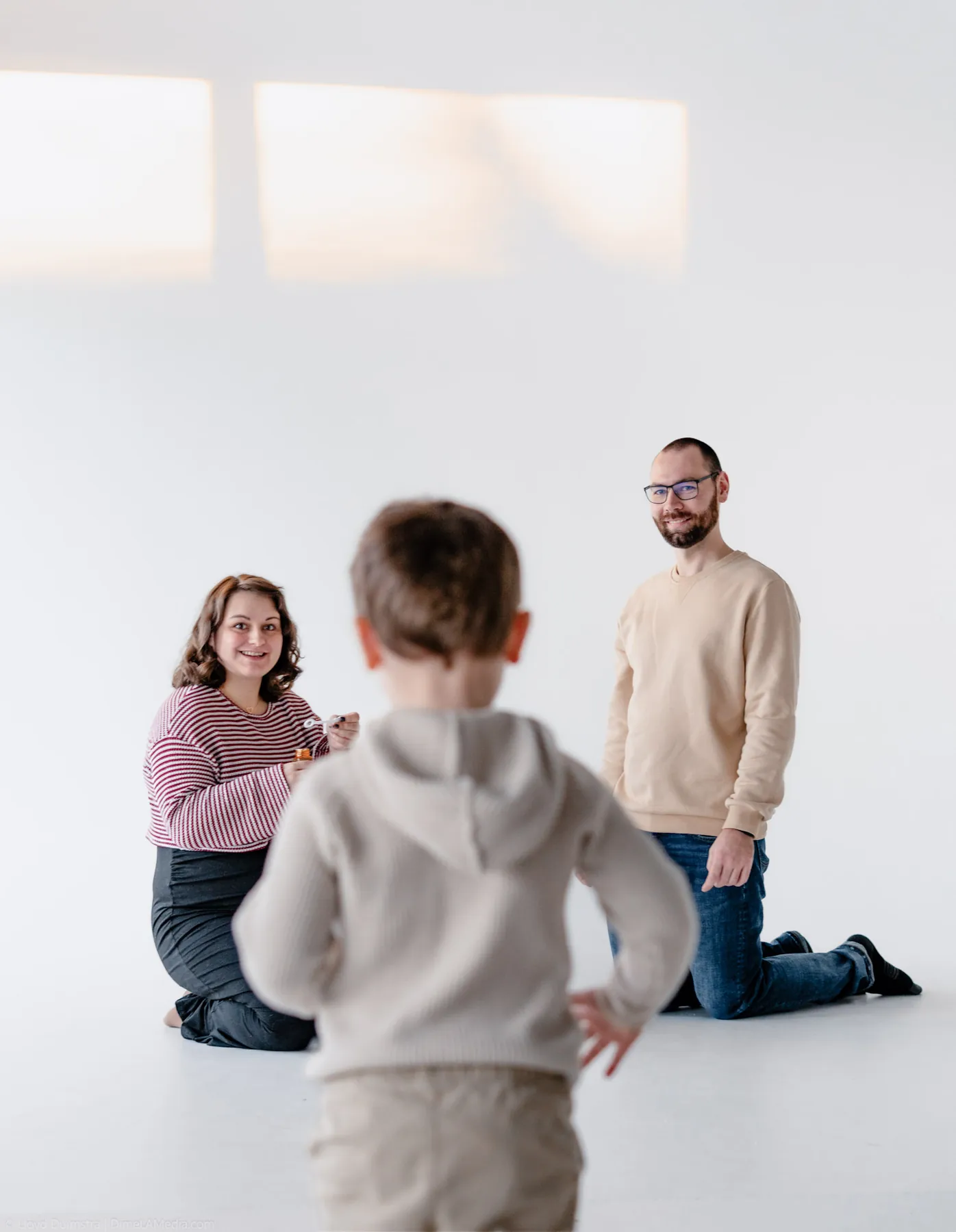 Studio maternity session with parents kneeling as their toddler runs between them