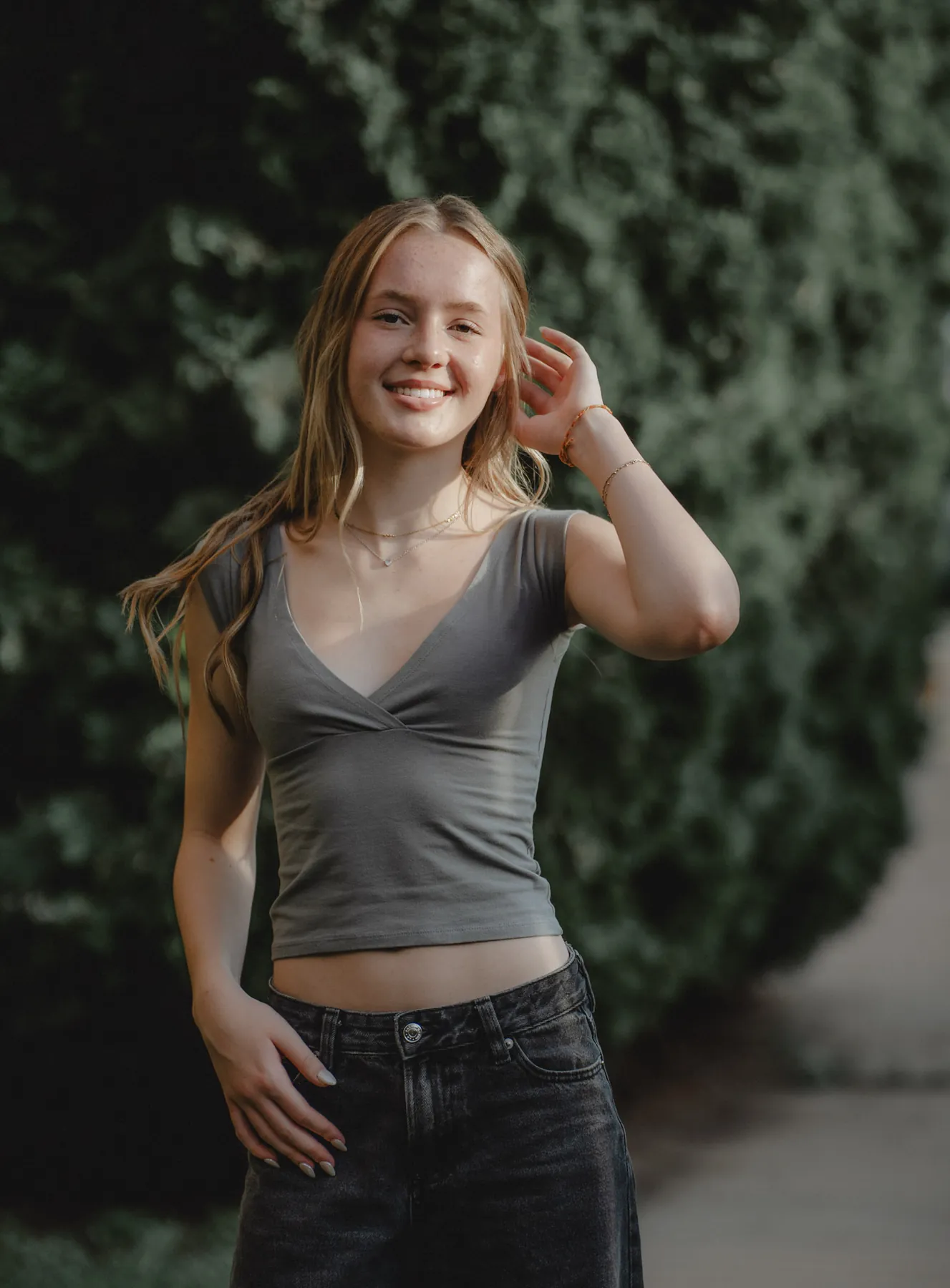 Scout smiling with a hand in her hair in front of evergreens, Sioux Falls senior session