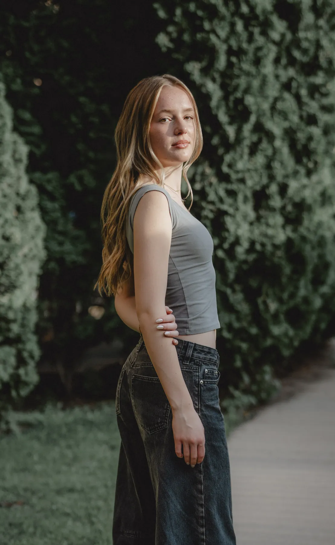 Senior portrait in profile against a dark evergreen hedge