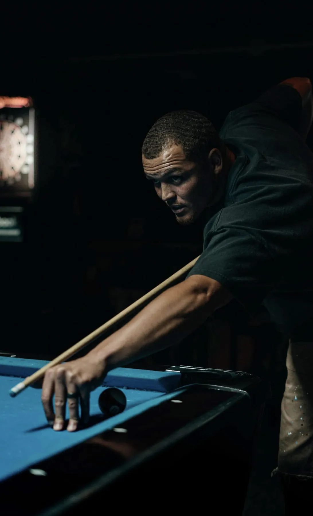 Low-key portrait over a pool table with dartboard glow
