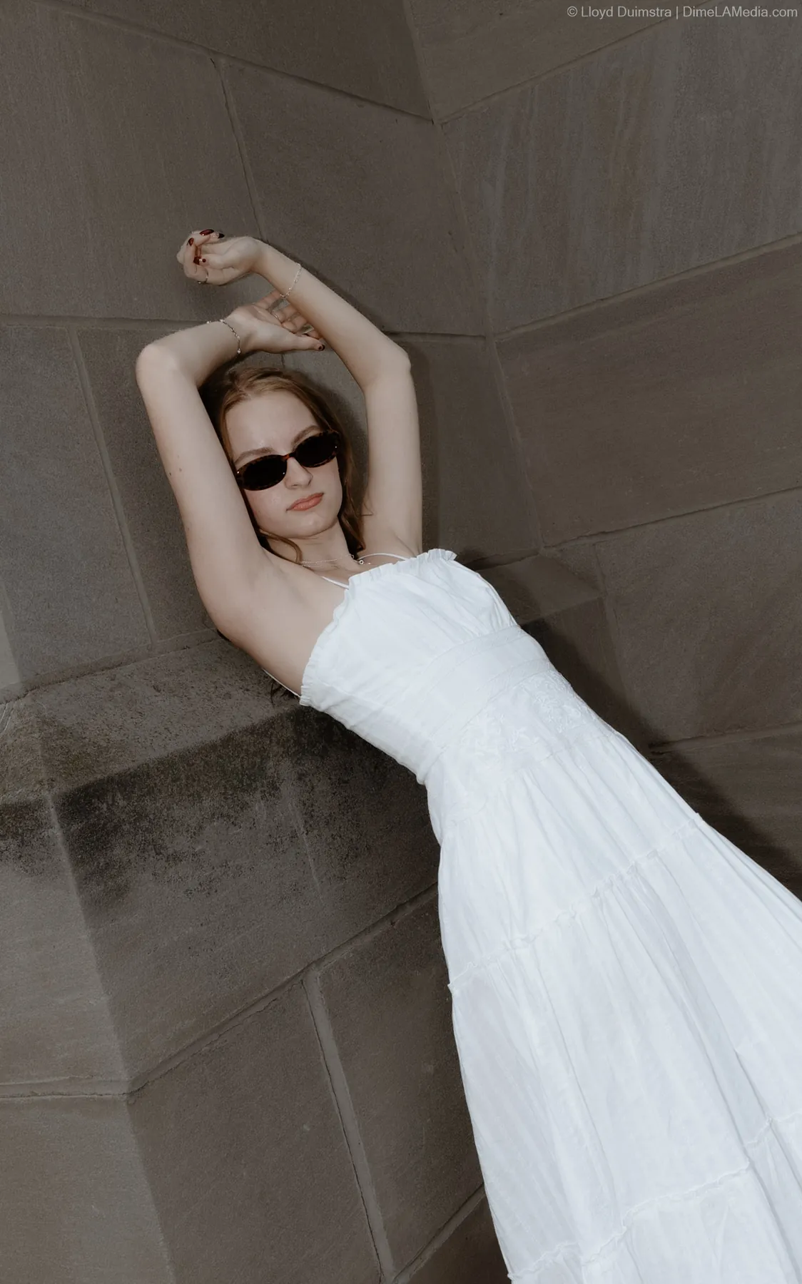 Syd Patzwald in a white dress reclining on a stone ledge