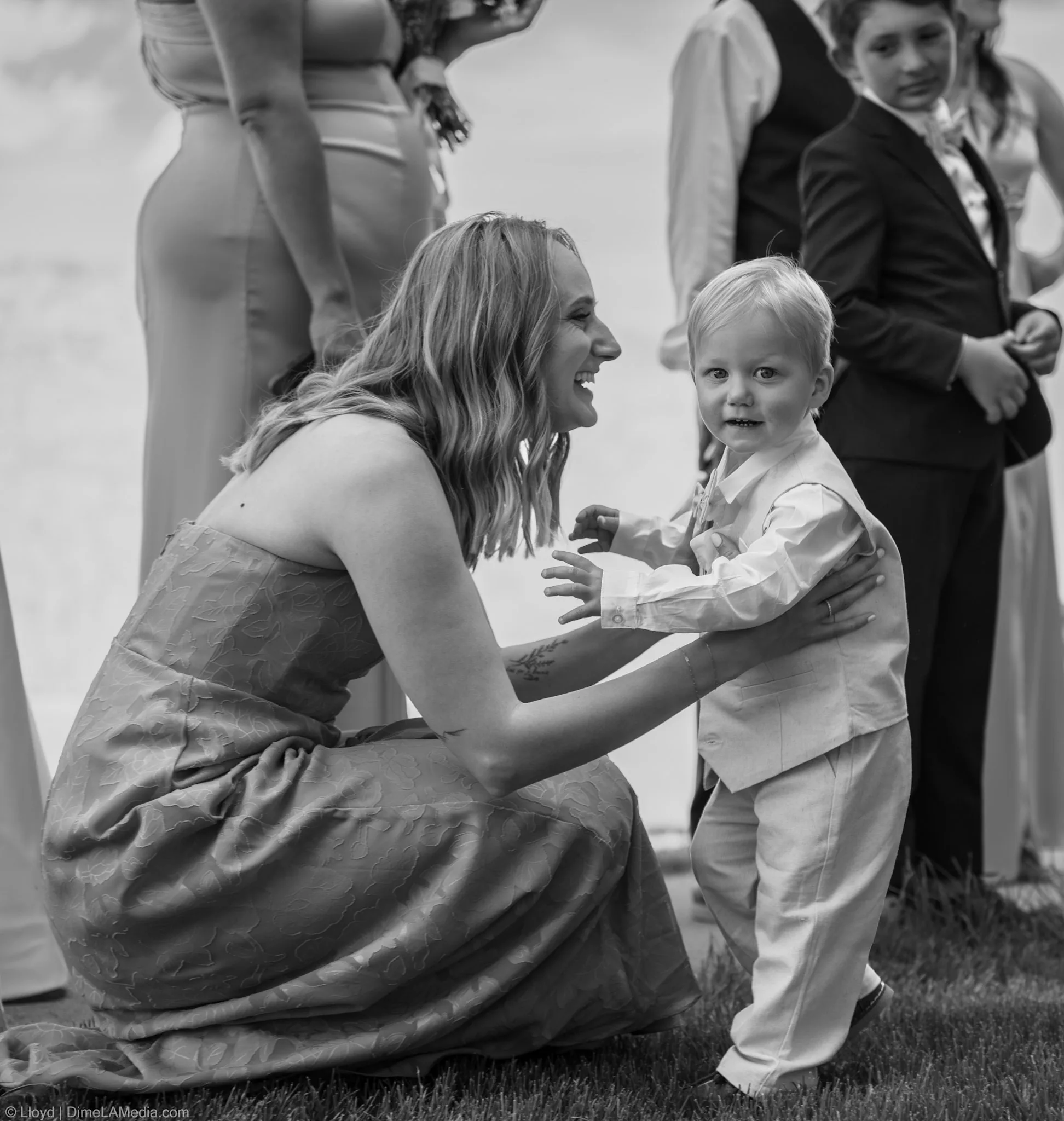 Bridesmaid kneeling down to hug the ring bearer before the ceremony, black and white