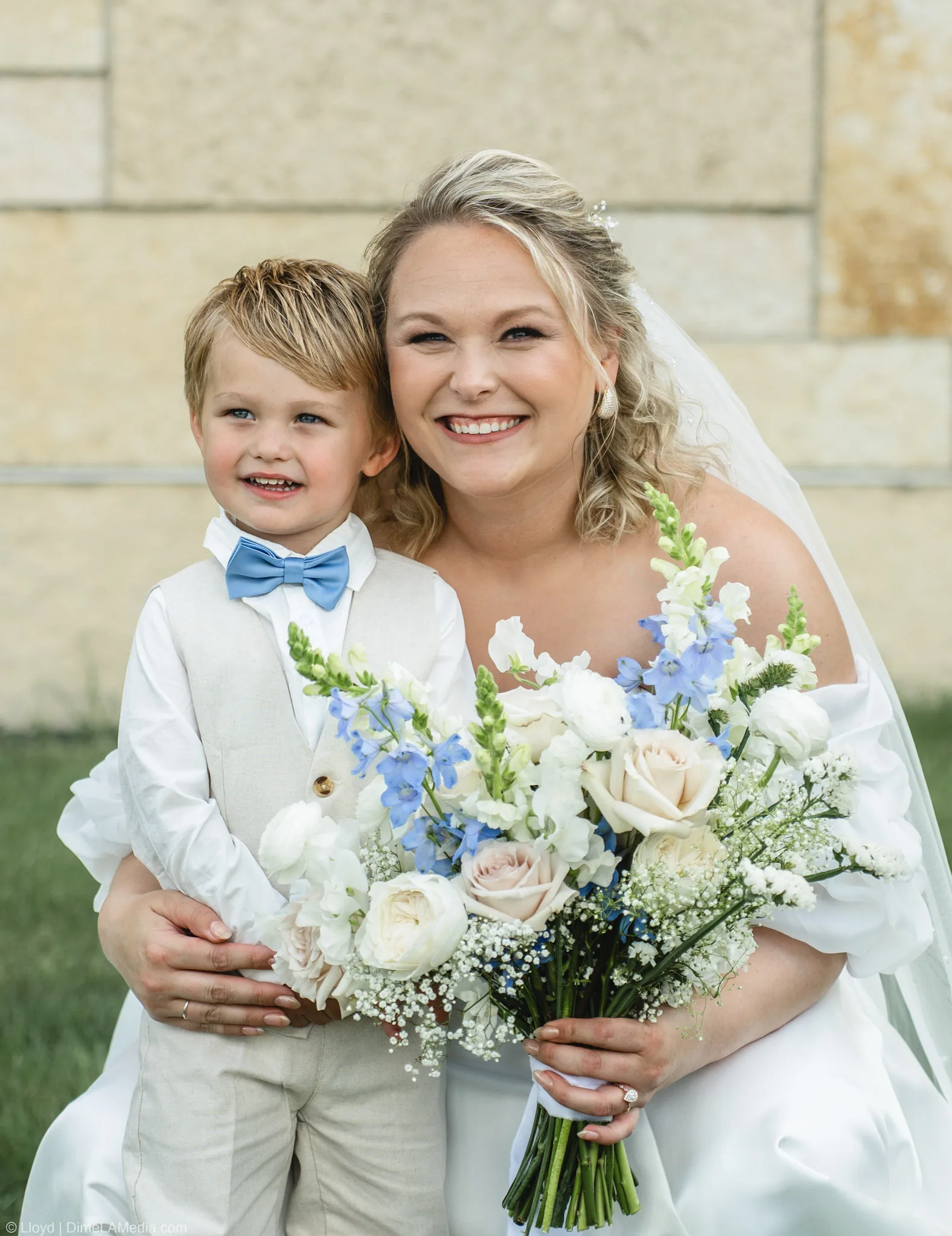 Bride hugging the ring bearer close, both of them smiling behind her blue and white bouquet