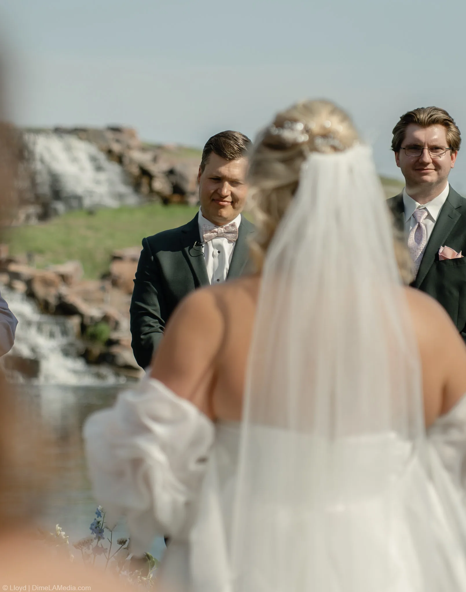 Bride's view down the aisle toward her groom and his groomsman beside the quarry waterfall