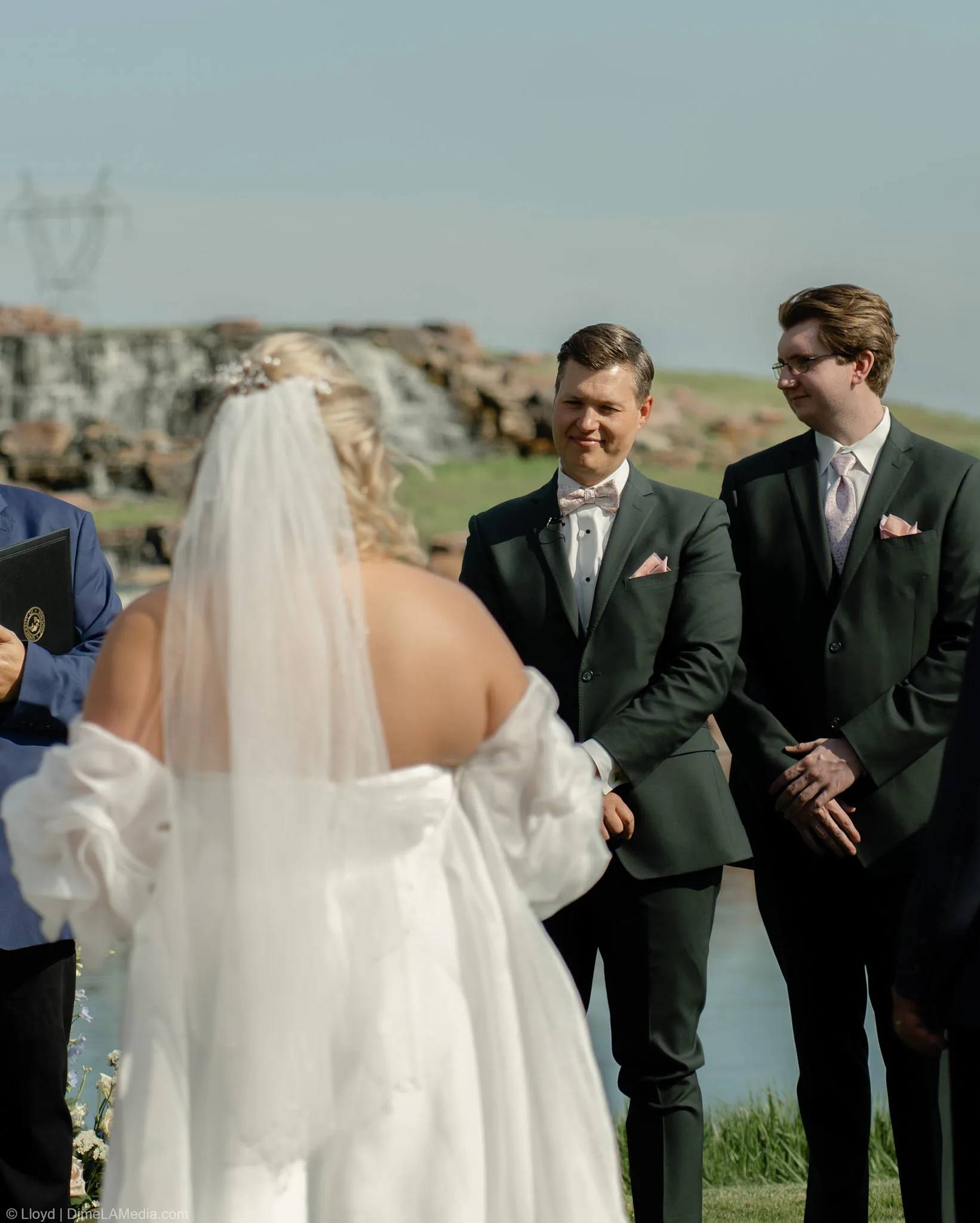 Bride facing her groom and the officiant at an outdoor ceremony beside a waterfall