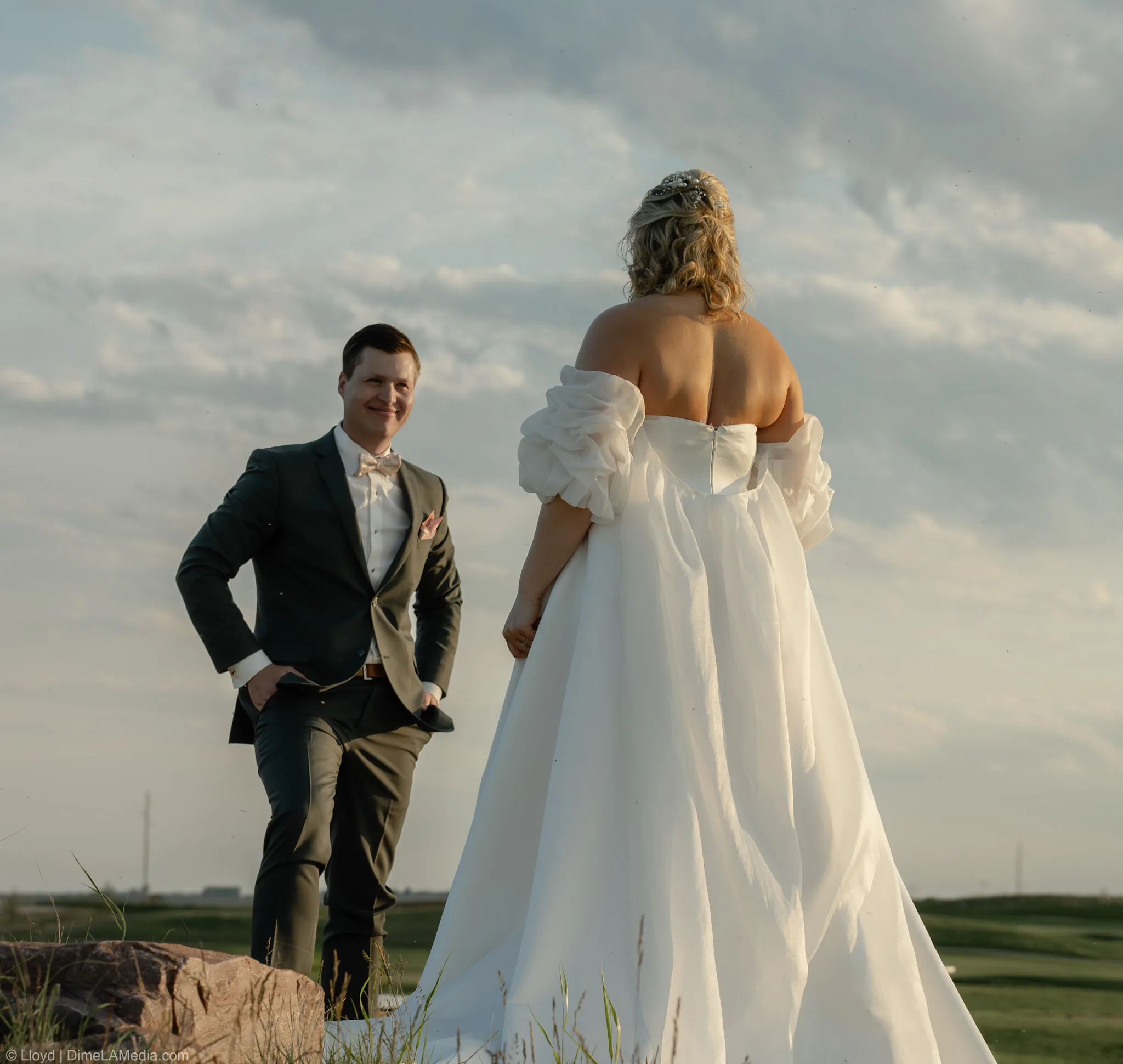 Groom looking back at his bride on a rock outcrop at golden hour under big prairie clouds