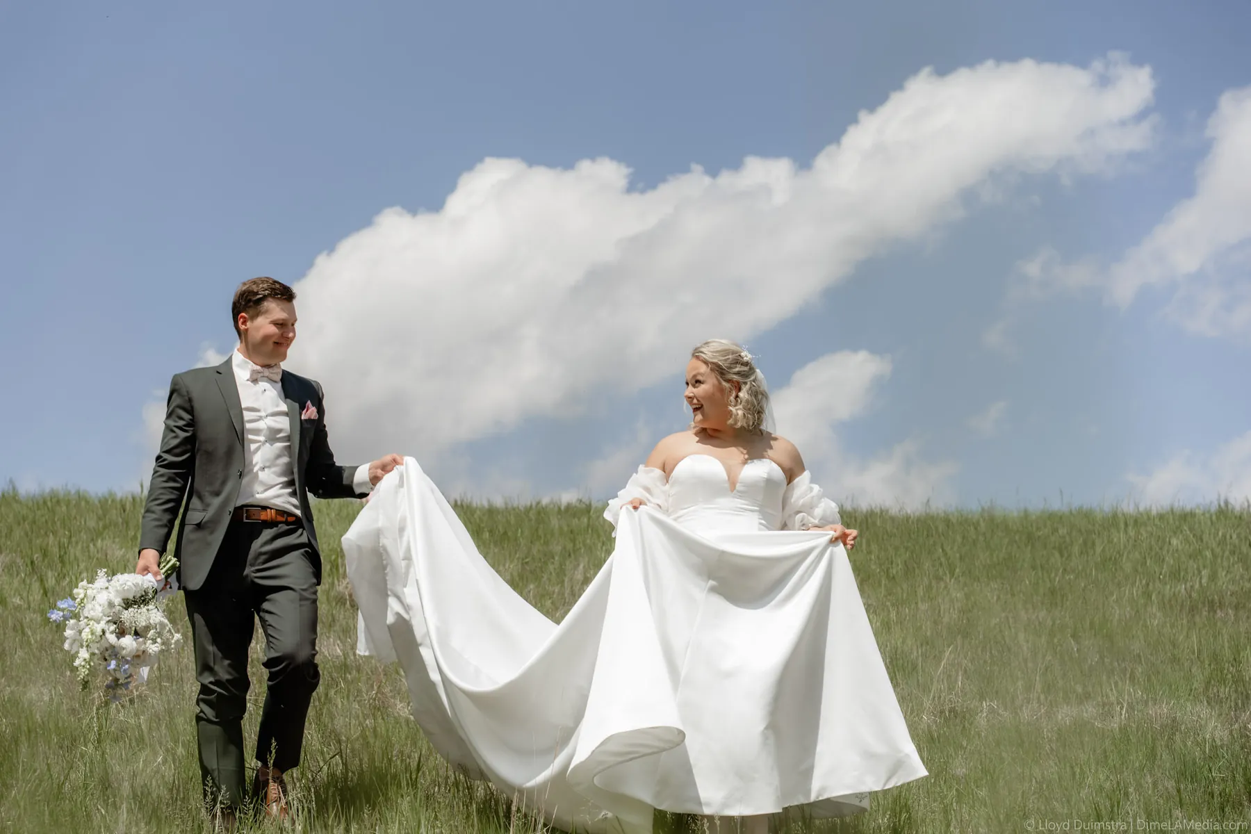Bride carrying her train through the grass under big prairie clouds, Sioux Falls SD
